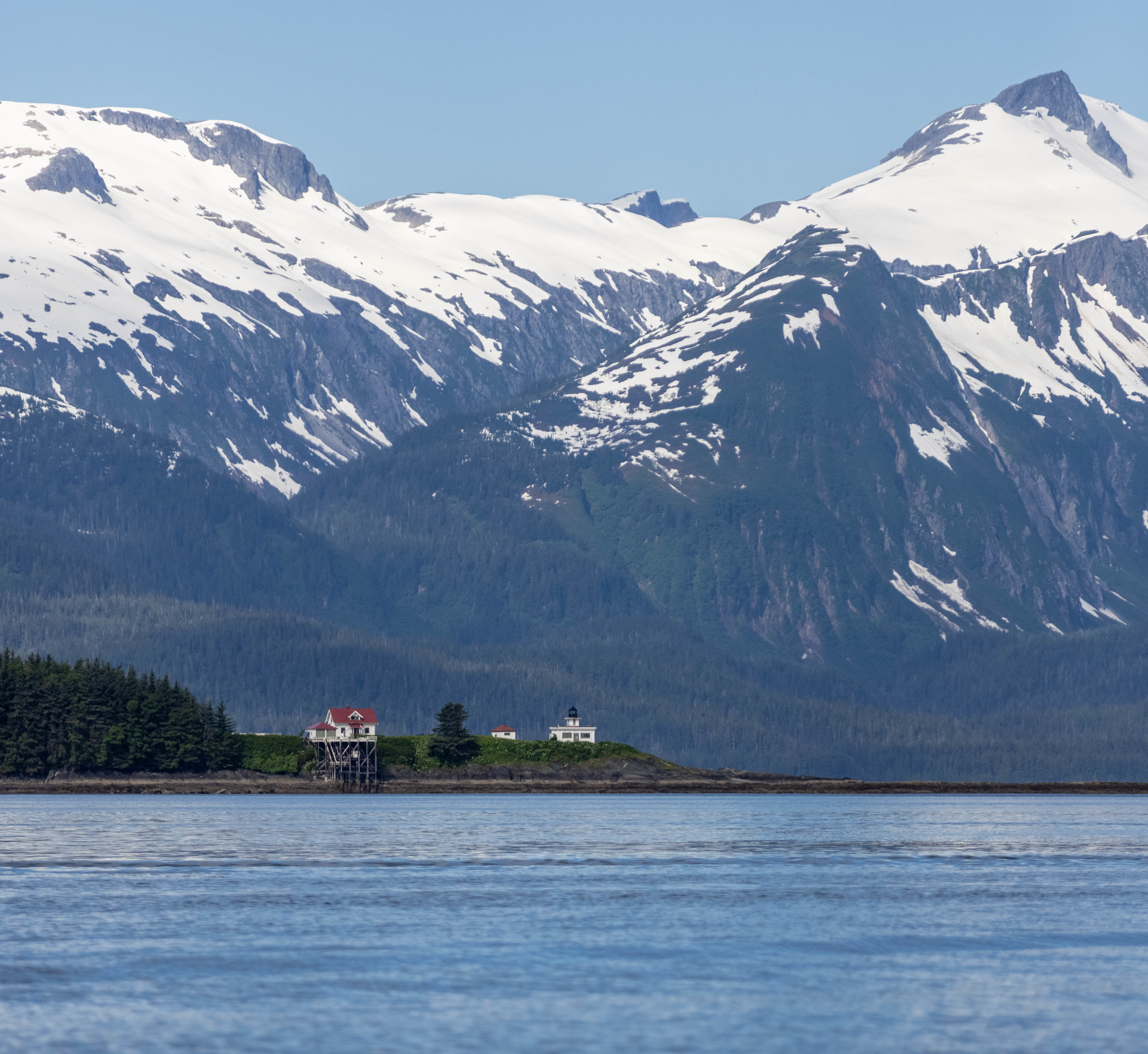 A lighthouse on an island in Alaska with mountains in the background 