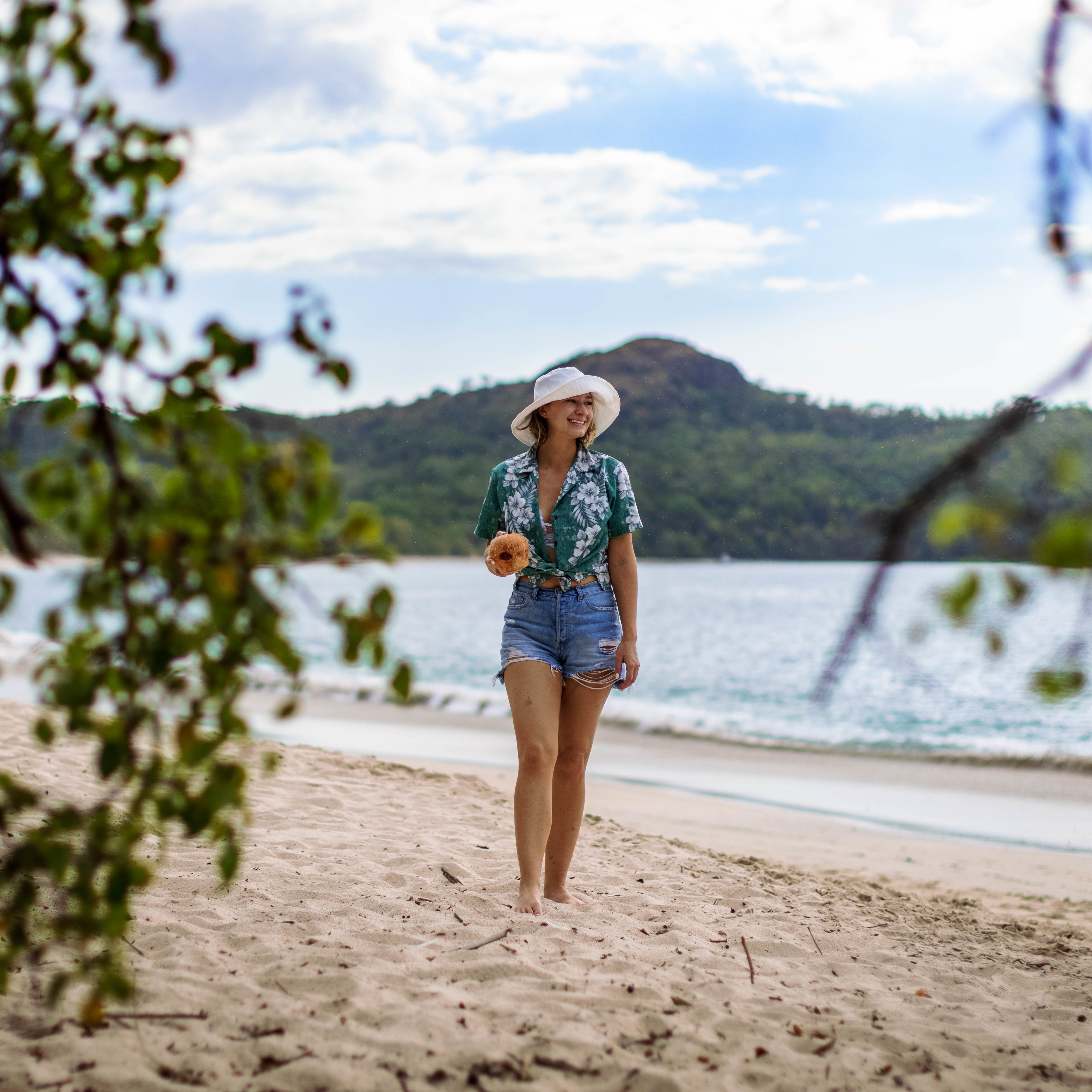 A woman wearing a Hawaiian shirt and jeans shorts walks along the beach in Costa Rica. Outfit is part of a Costa Rica vacation lookbook.