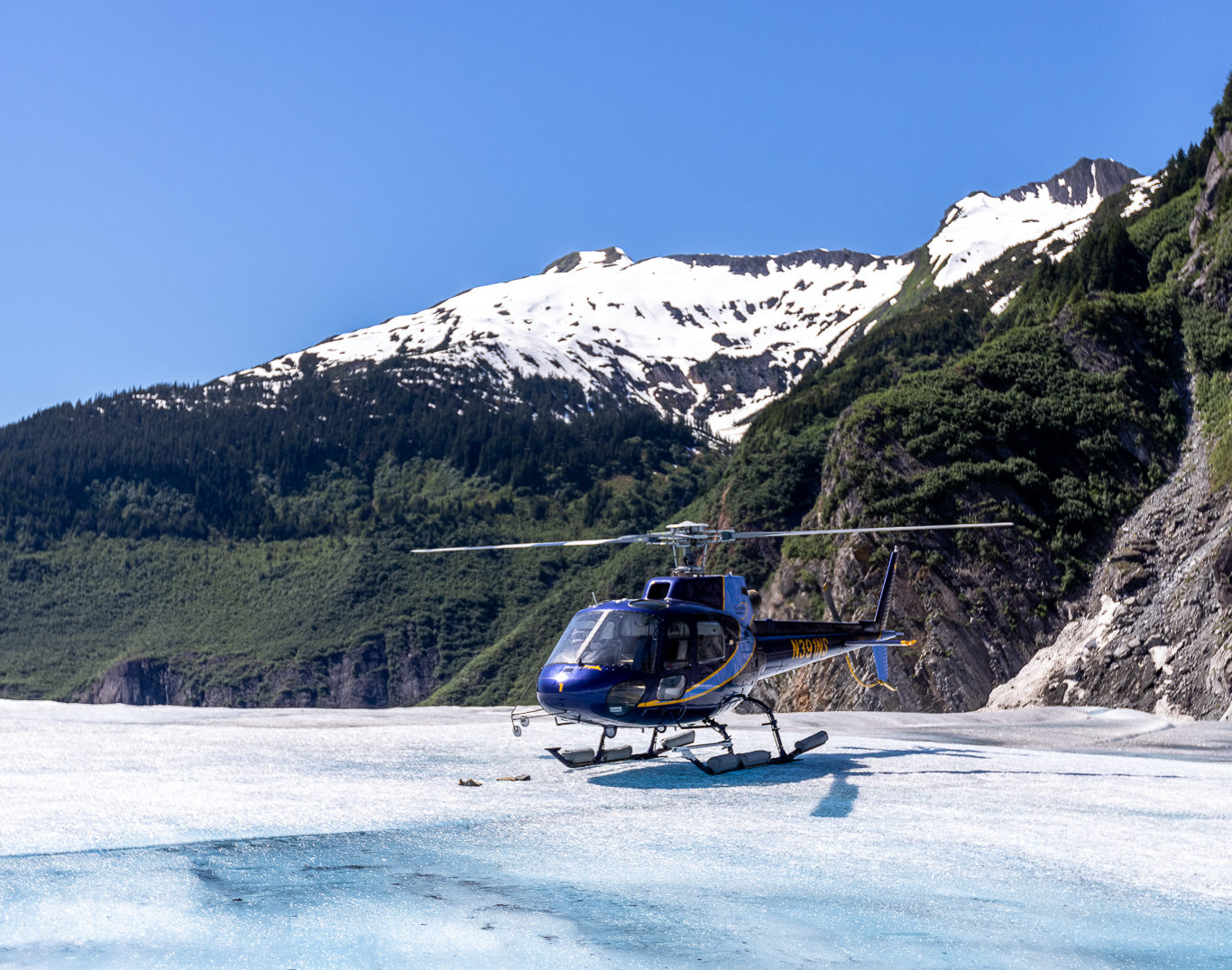 A blue NorthStar Helicopter on a glacier with a snow capped mountain in the background