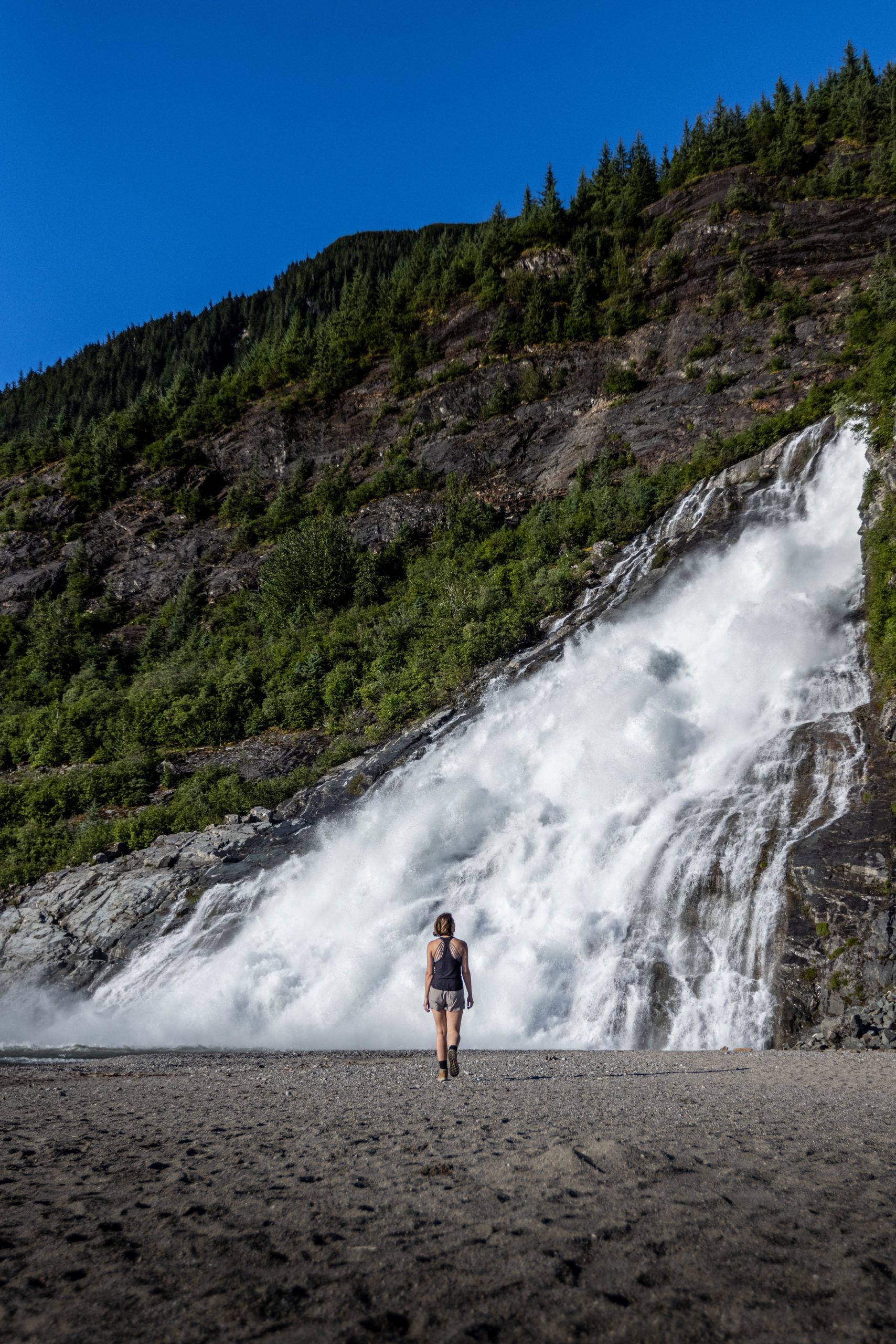 Lindsay, One Girl Wandering, stands in front of Nugget Falls in Juneau, Alaska