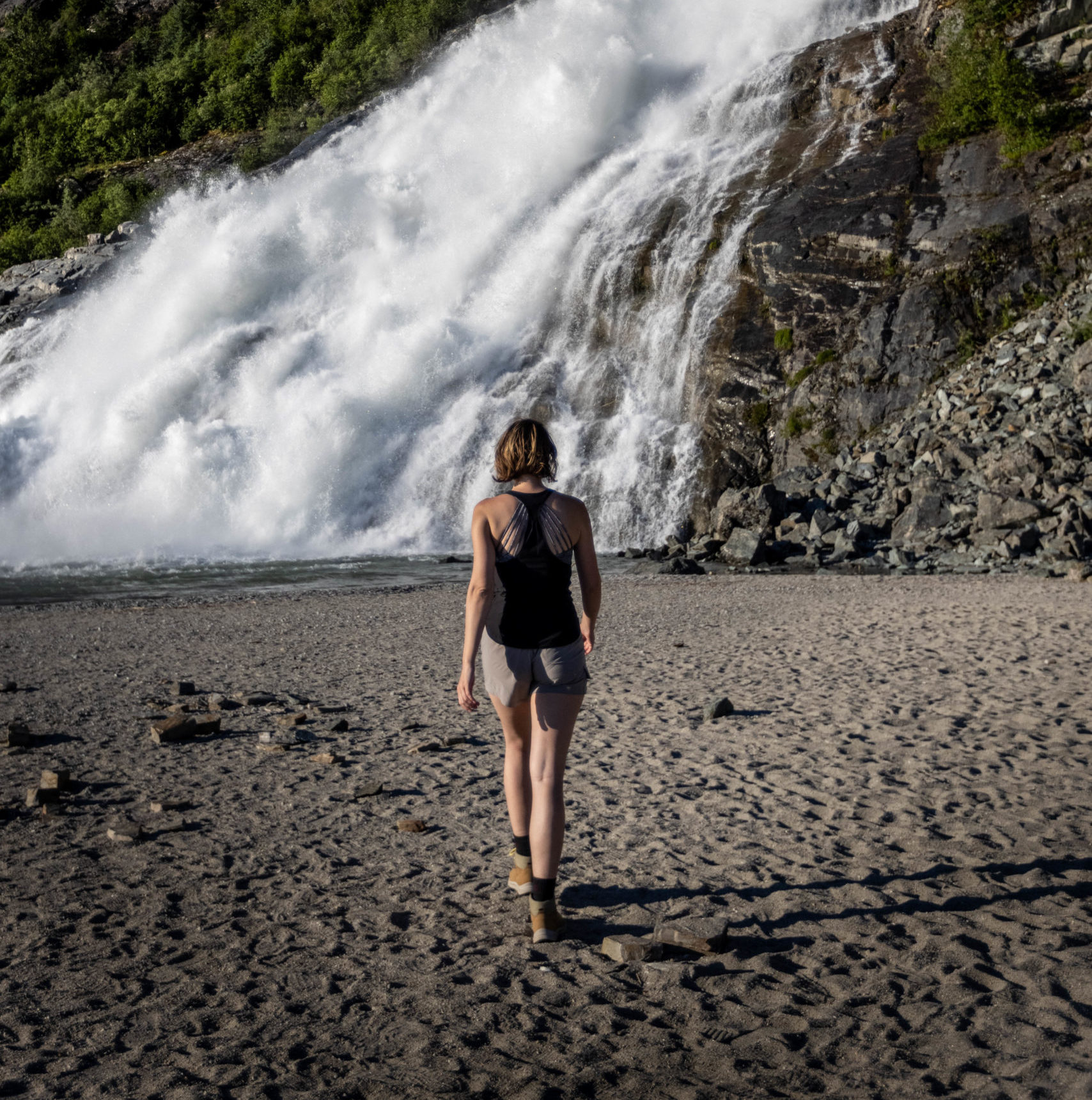A woman in athletic clothing walks towards Nugget Falls in Juneau Alaska. Don't forget to add clothing for activites to your Alaska packing list.