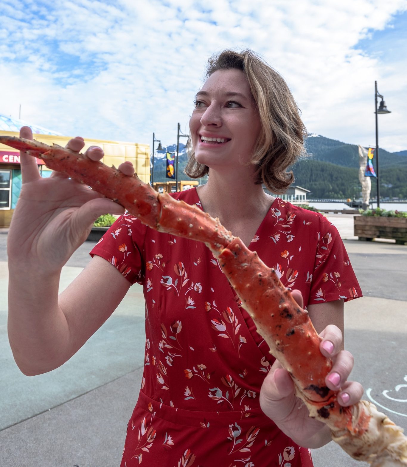 Don't forget to add a dress to your Alaska packing list. A woman in a red dress holds a large king crab leg in Juneau Alaska.