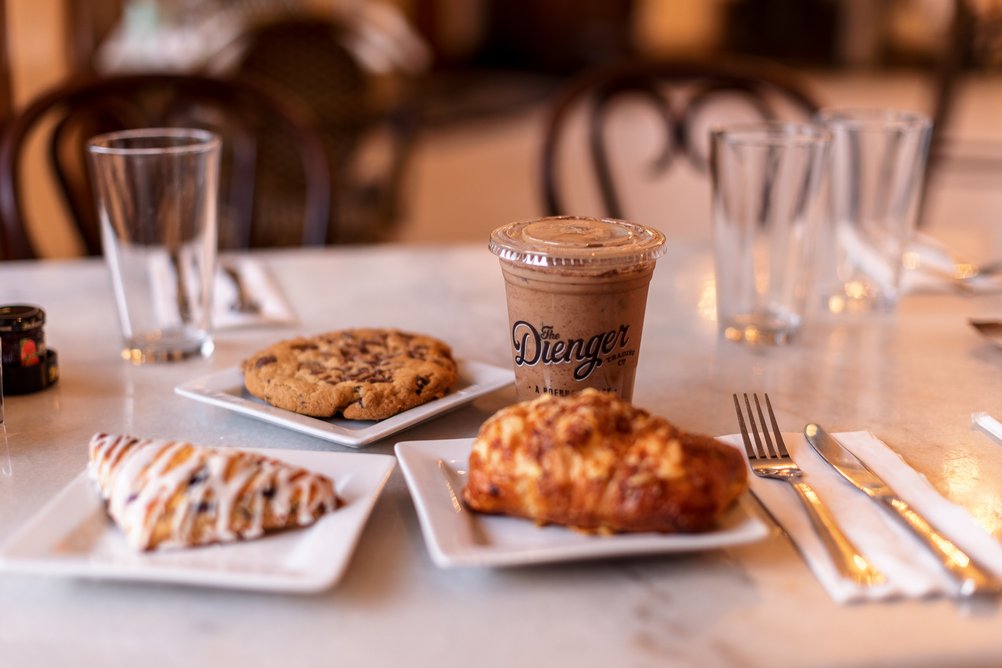 A iced coffee, scone, ham and cheese croissant, and a cookie on a table at The Dienger Trading Co. in Boerne, TX.